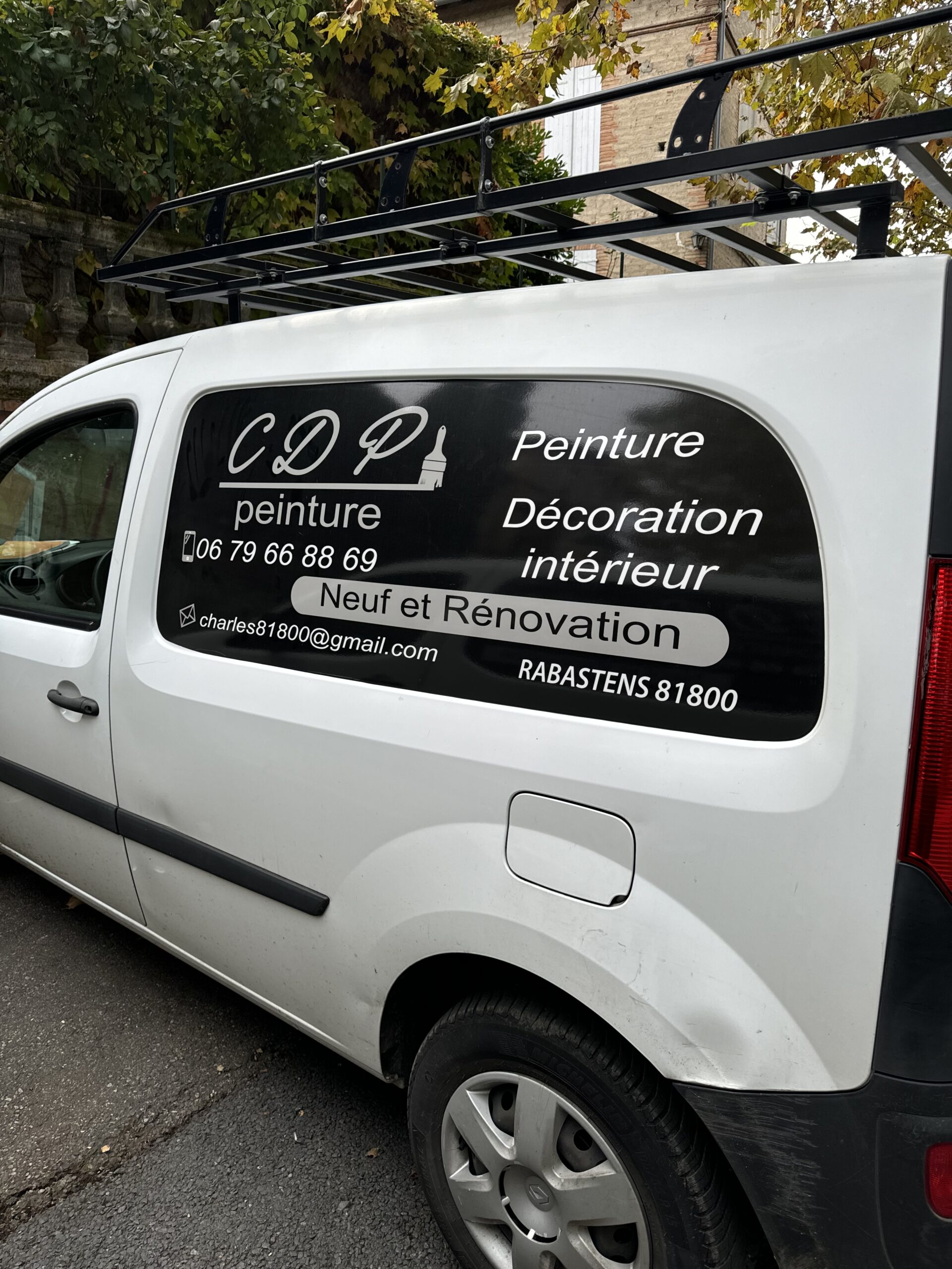 Arrière d'un fourgon blanc, floqué du logo "CDP Peinture". Les coordonnées de l'entreprise, ainsi que les services proposés (peinture, décoration intérieure, rénovation) sont clairement indiqués en noir sur fond blanc.