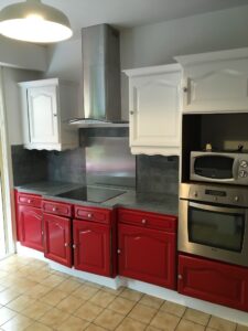 Cuisine lumineuse avec des armoires murales blanches et des armoires basses rouges, créant un espace dynamique et chaleureux. Le plan de travail en granit gris ajoute une touche d'élégance, tandis que les appareils électroménagers en inox apportent une finition moderne